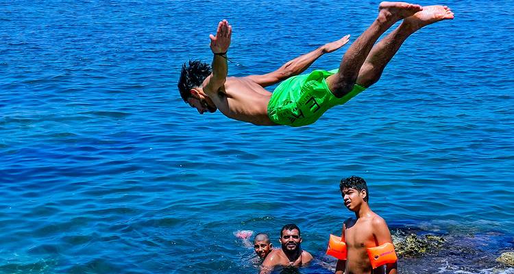 Personne plongeant dans la mer près d'un groupe de personnes.