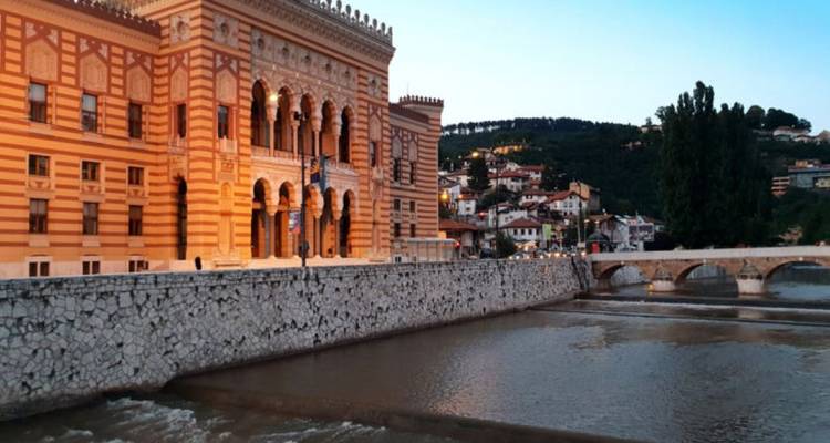 Edificio histórico con un río y colinas al fondo.