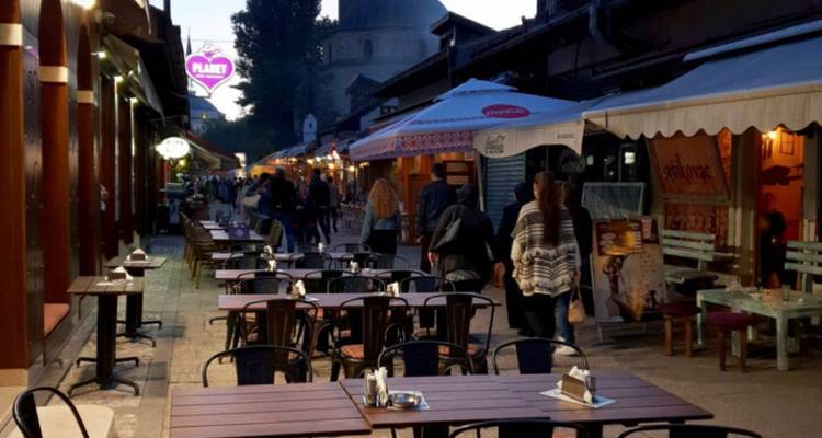 Calle exterior con mesas y gente caminando.