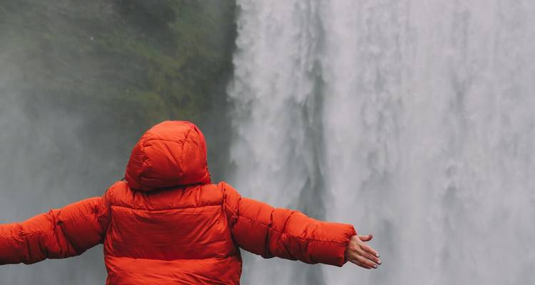 Persoon in een oranje jas die naar een grote waterval kijkt.