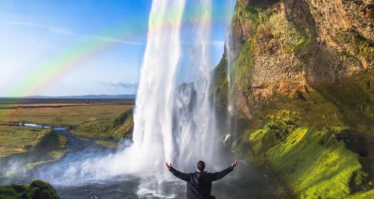Persoon die staat voor Seljalandsfoss waterval met een regenboog.