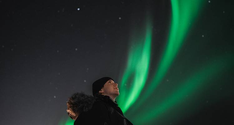 Persoon onder het noorderlicht in een donkere hemel.