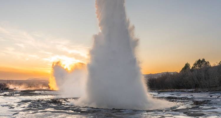 Geiser die uitbarst bij zonsondergang met opstijgende stoom.