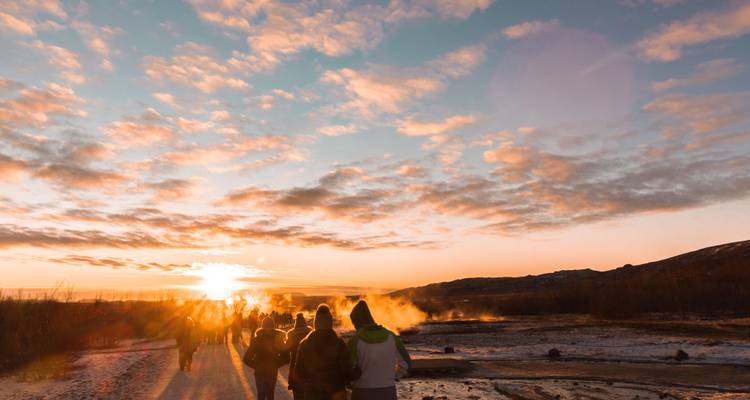 Groep mensen die bij zonsopgang naar een dampend geothermisch gebied lopen.