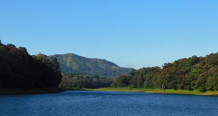 Meer omringd door beboste heuvels onder een heldere blauwe hemel.