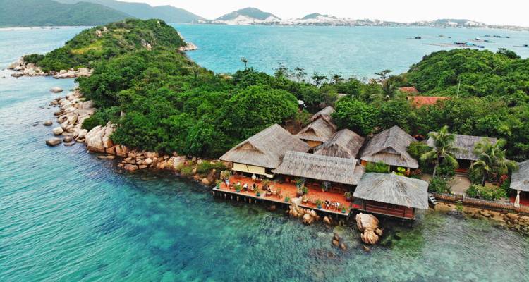 Luftaufnahme eines abgelegenen Inselresorts, umgeben von klarem, türkisfarbenem Meer und üppiger Vegetation.
