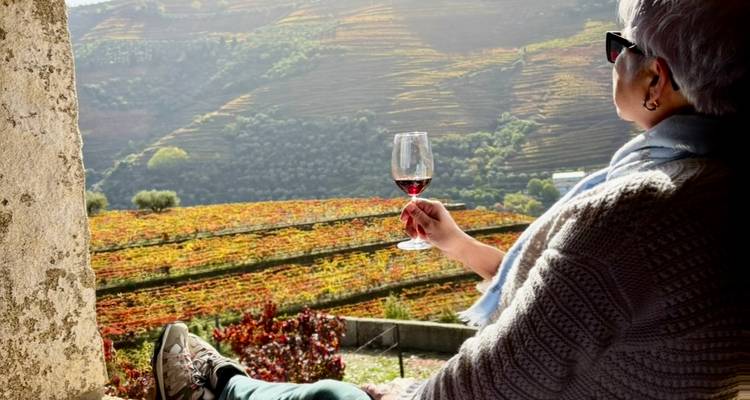 Une femme savourant un verre de vin avec vue sur le vignoble dans la vallée du Douro.