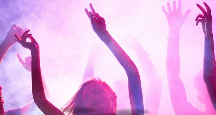 Des gens dansant avec les mains levées dans une lumière colorée.