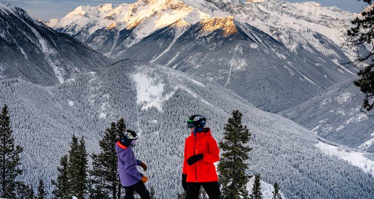 Deux skieurs en tenues colorées sur une montagne enneigée avec de beaux sommets en arrière-plan.
