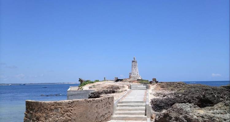 Monument côtier sur un rivage rocheux avec un ciel bleu et l'océan en arrière-plan.