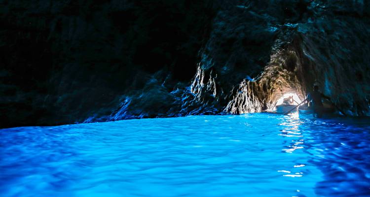 Inside the luminous Blue Grotto where turquoise water glows under a dark cave ceiling with a small boat at the lighted entrance.