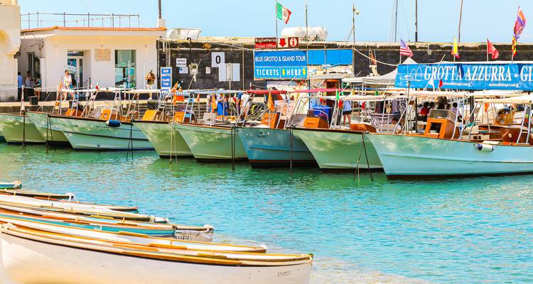 Row of colourful excursion boats moored in the clear turquoise harbour of Capri under bright sunlight.