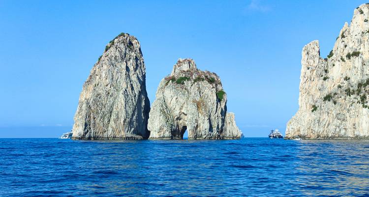 Iconic Faraglioni limestone sea stacks rising dramatically from deep blue Mediterranean waters.