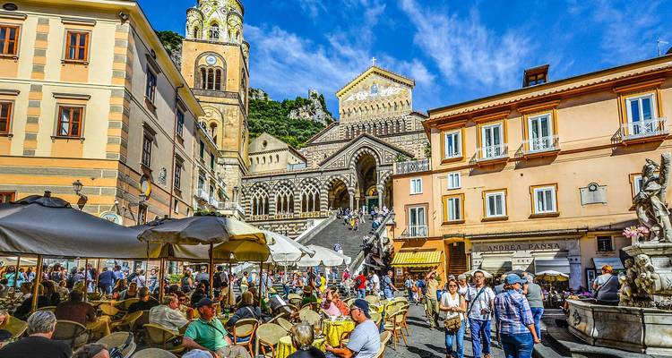 Bustling Piazza del Duomo in Amalfi with cafés and the ornate cathedral facade towering above crowds.