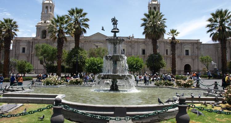 Una plaza concurrida con una fuente central y una iglesia de la época colonial.