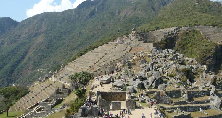Vista de antiguas terrazas de piedra en una ladera montañosa con turistas explorando.
