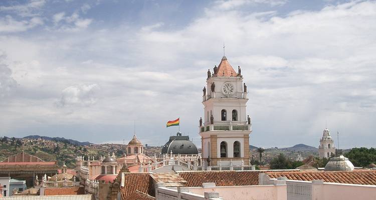 Panoramablick vom Dach auf Sucre mit einem Uhrenturm und einer bolivianischen Flagge, die über Terrakottadächern weht.