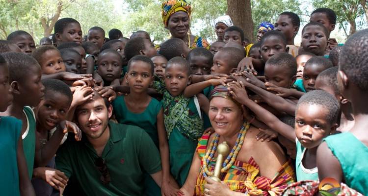 Grupo de niños y adultos sonriendo a la cámara en un entorno rural.