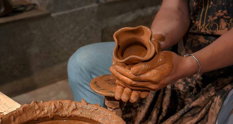 Persona moldeando arcilla en un torno de alfarería en un entorno artesanal.