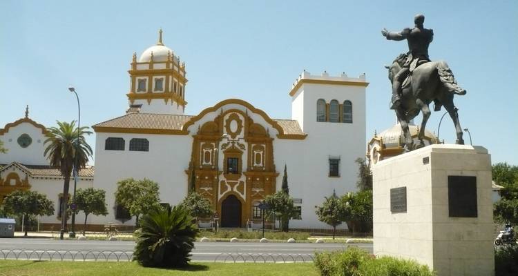 Statue et bâtiment historique le long d'une rue bordée d'arbres.
