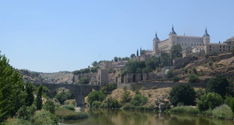 Vue panoramique d'une ville historique avec un grand château surplombant une rivière.