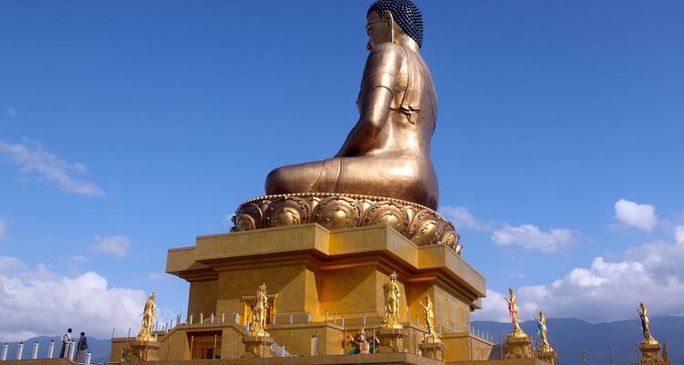 Une grande statue dorée de Bouddha avec de petites silhouettes debout à proximité