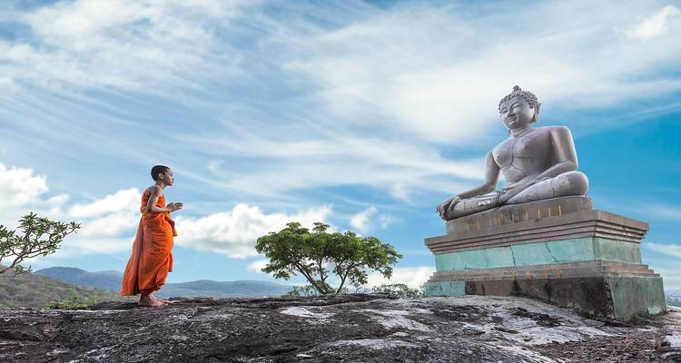 Jeune moine en robes orange debout devant une grande statue de Bouddha