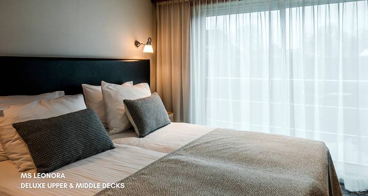 Innenraum einer Kreuzfahrtschiff-Kabine mit einem ordentlich gemachten Bett und großem Fenster.