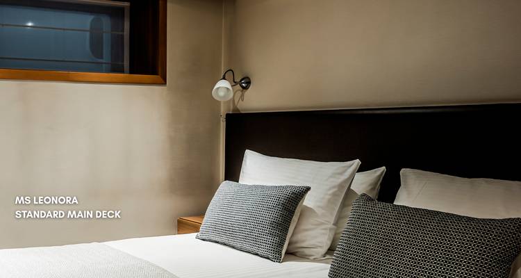 Innenraum einer Kabine auf einem Kreuzfahrtschiff mit einem Bett und einer Wandlampe.