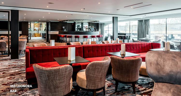 Barbereich im Inneren eines Kreuzfahrtschiffs mit roten Sitzgelegenheiten und Tischen.