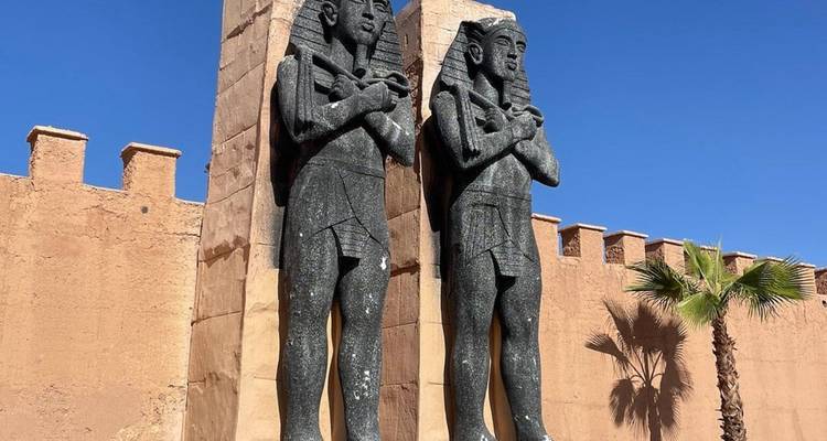 Standbeelden van oude Egyptische figuren bij een ingang met palmbomen.