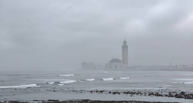 Mistige kust met een prominente moskee en oceaangolven.