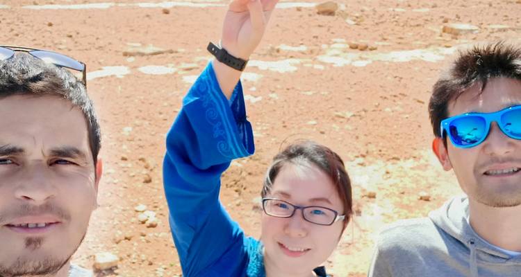 Selfie of three travelers under bright sun on a rocky desert plain.
