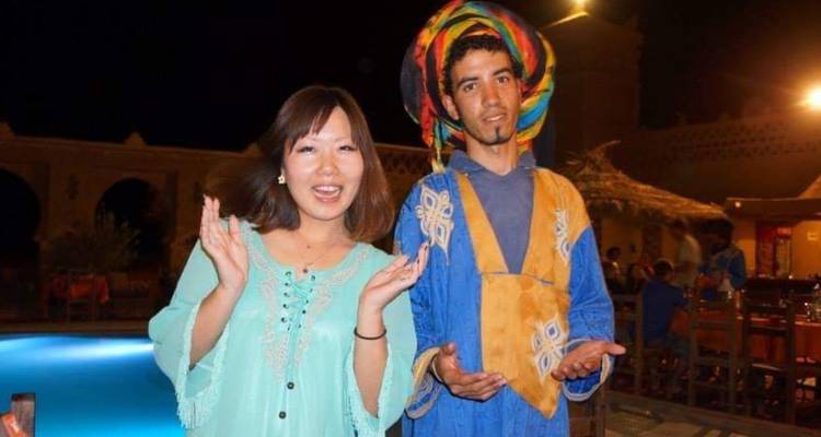 Smiling woman clapping next to brightly dressed entertainer beside a lit pool at night.