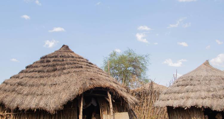 Huttes traditionnelles au toit de chaume sous un ciel bleu dégagé.