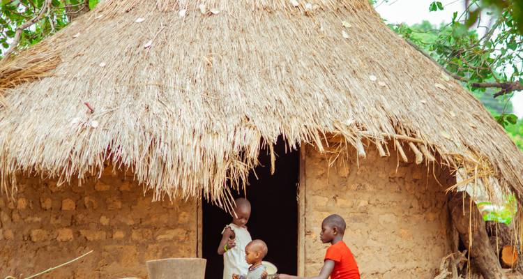 Des enfants jouent dehors près d'une hutte au toit de chaume.