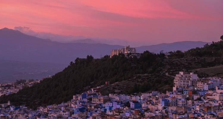 Stadtlandschaft von Chefchaouen bei Sonnenuntergang mit Gebäuden und einem rosa Himmel.