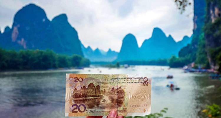 Un billet de 20 yuans tenu devant un paysage de montagnes karstiques.
