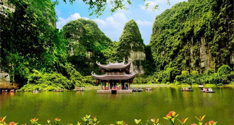 Pagoda tradicional rodeada de exuberante vegetación y montañas de piedra caliza reflejadas en el agua.