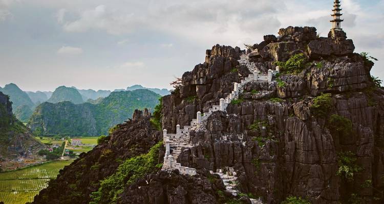 Colina rocosa con una escalera serpenteante y una pagoda de piedra alta que domina valles exuberantes.