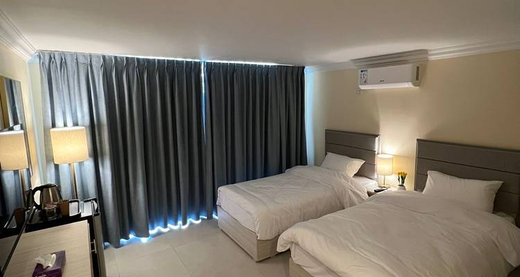 Einfaches Hotelzimmer mit zwei Einzelbetten, grauen Vorhängen und moderner Beleuchtung