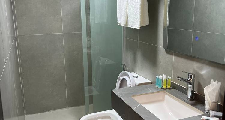 Modernes Hotelbadezimmer mit Glasdusche, grauen Fliesen und ordentlich angeordneten Annehmlichkeiten