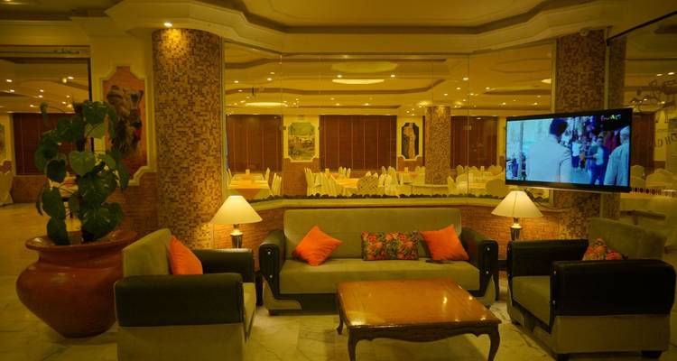 Warm beleuchtete Hotellobby mit Sofas, Mosaiksäulen und einem Fernseher an der Wand