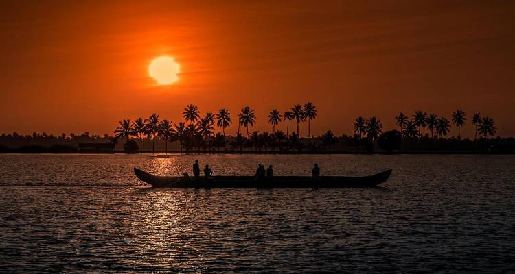 Silhouette d'un bateau contre un coucher de soleil vibrant avec des palmiers.