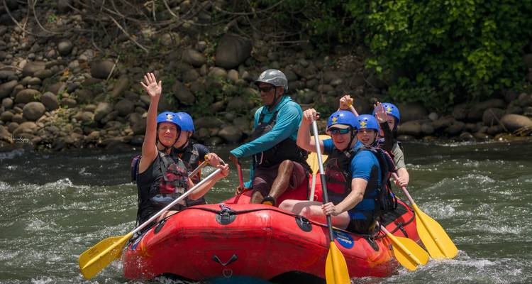 Wildwaterkajakkers peddelen door stroomversnellingen in een rode opblaasbare boot en zwaaien vrolijk