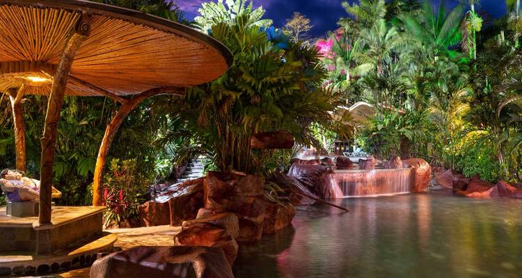 Weelderige tropische warmwaterbronnen resort 's nachts verlicht met waterval zwembaden en groene bladeren
