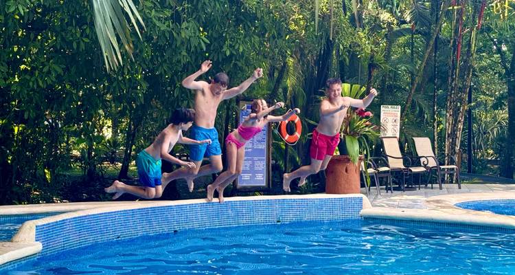 Familie van vier springt in een hotelzwembad omringd door weelderig groen