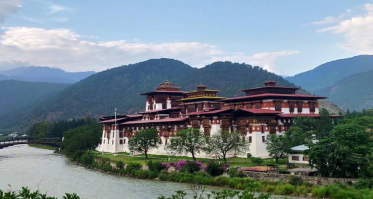 Grote Bhutanese dzong bij een rivier omringd door bergen.