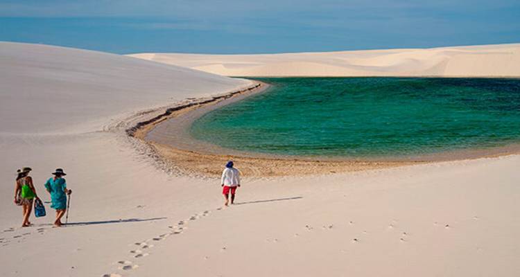 Witte zandduinen met heldere waterlagune en wandelende mensen.