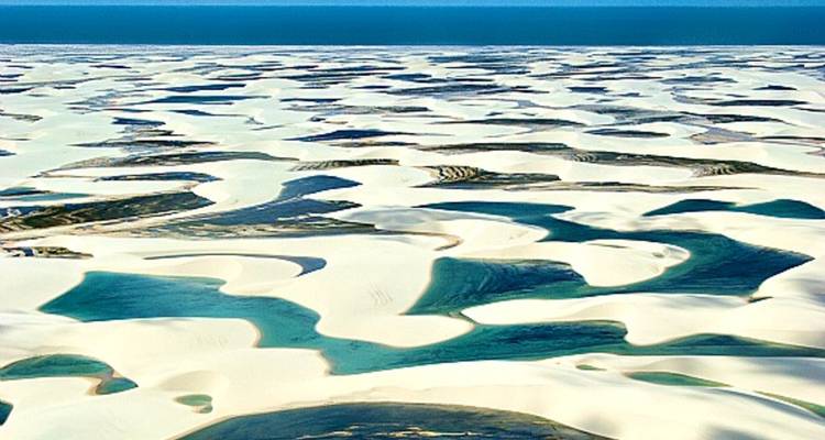 Uitgestrekt uitzicht op witte zandduinen en turquoise lagunes in een woestijn.